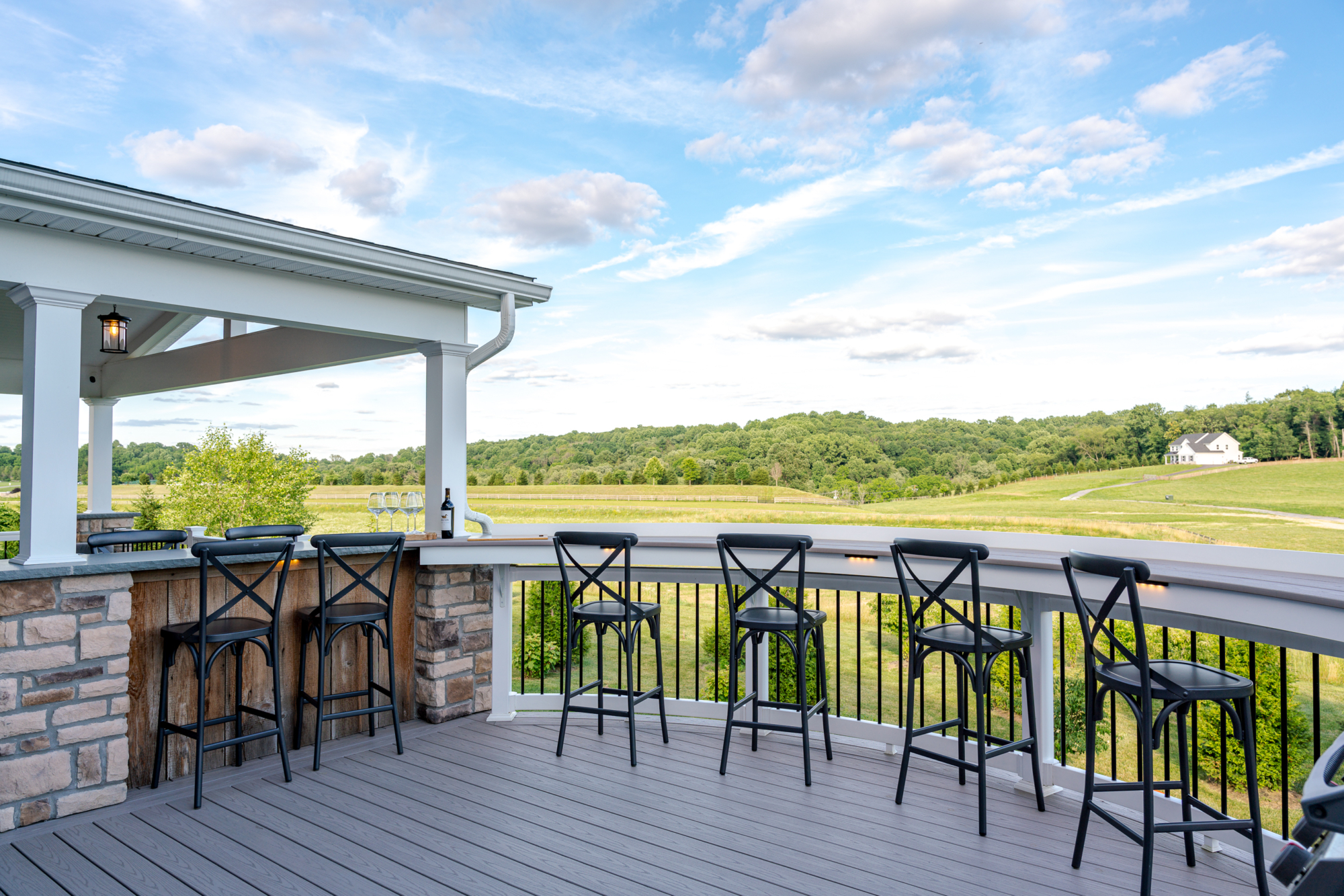 image of a deck in west bradford pa built by integrous fences and decks featuring a roof area a curved deck board bar timbertech decking and white vinyl railing with black aluminum balusters