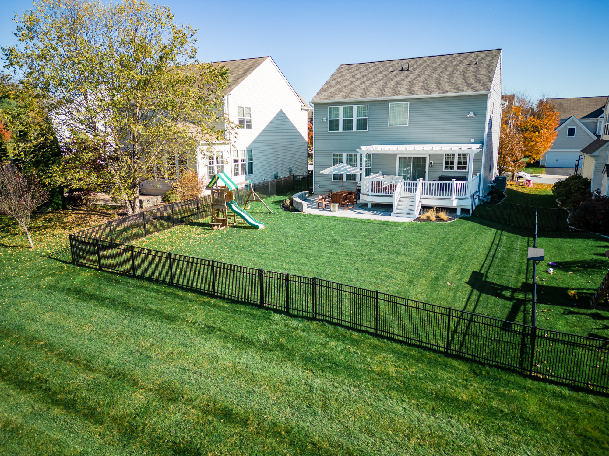 image of a deck and patio in downingtown pa built by integrous fences and decks featuring a white vinyl pergola timbertech decking white vinyl railing paver patio and sitting wall around the yard is a black aluminum fence
