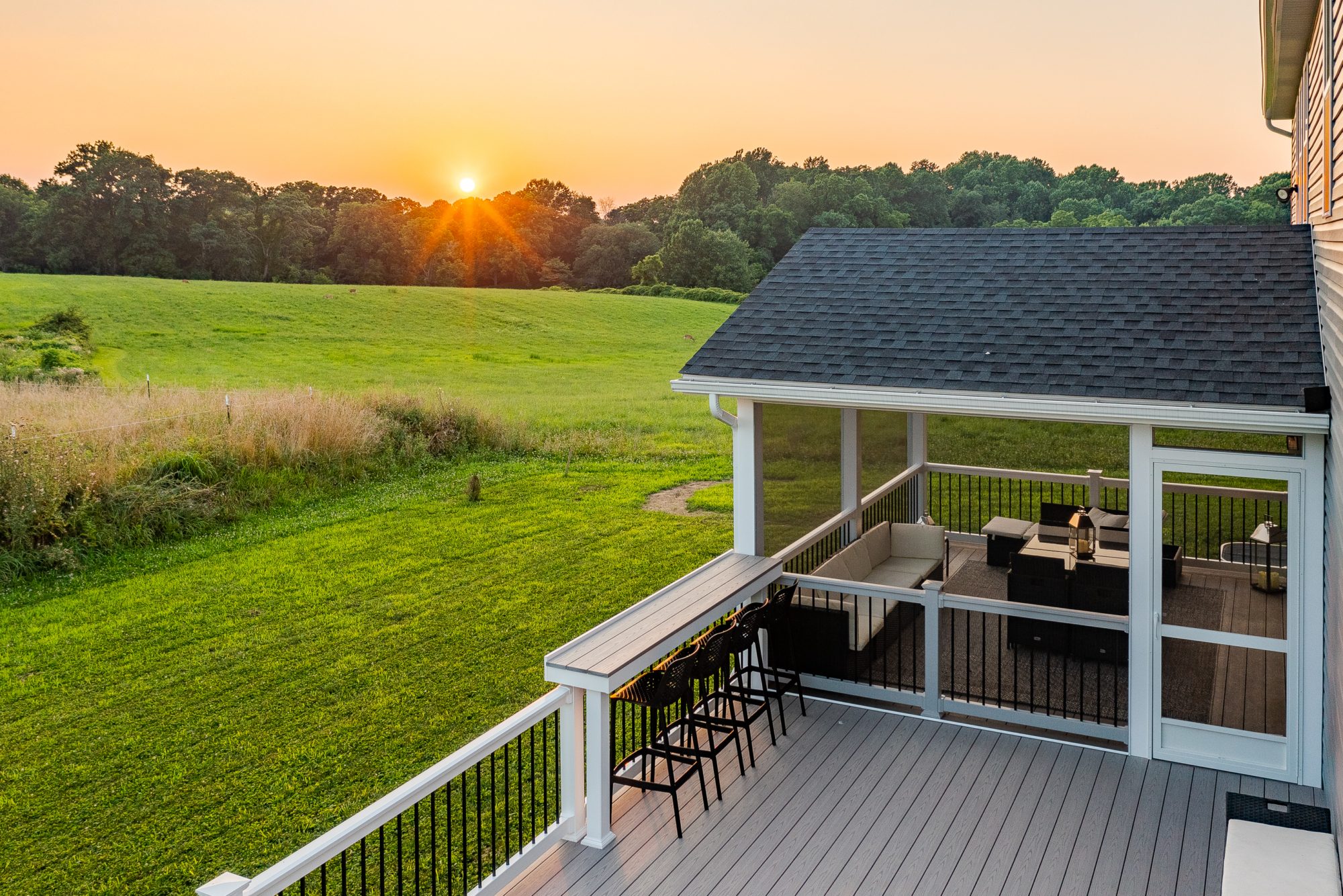 image of a deck with a screened in roof in avondale pa built by integrous fences and decks featuring a deck board bar timbertech decking and white vynl railing with black aluminum balusters