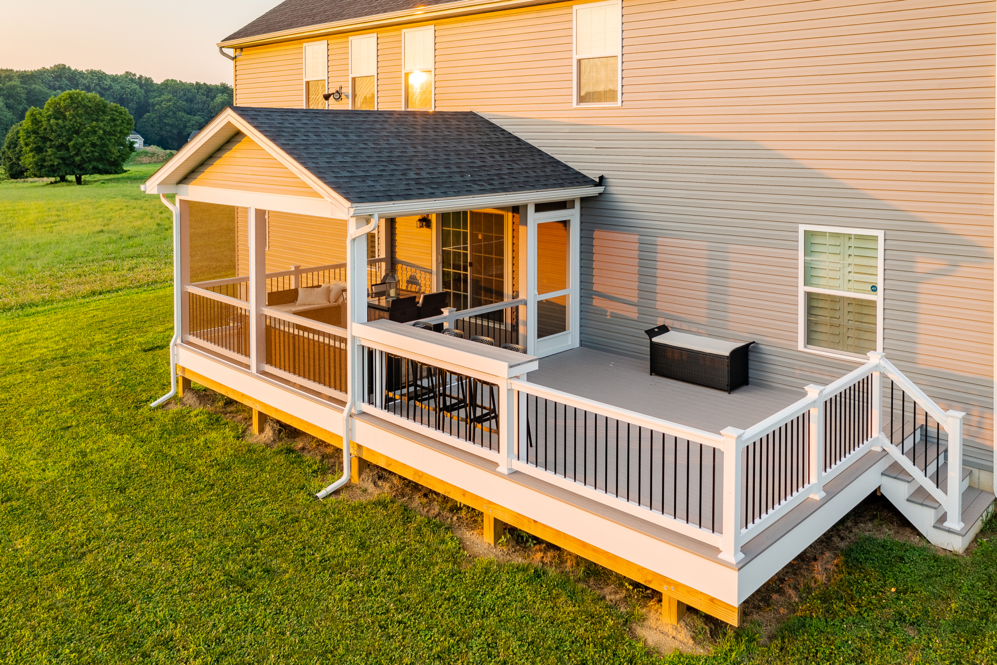 image of a deck with a screened in roof in avondale pa built by integrous fences and decks featuring a deck board bar timbertech decking and white vynl railing with black aluminum balusters