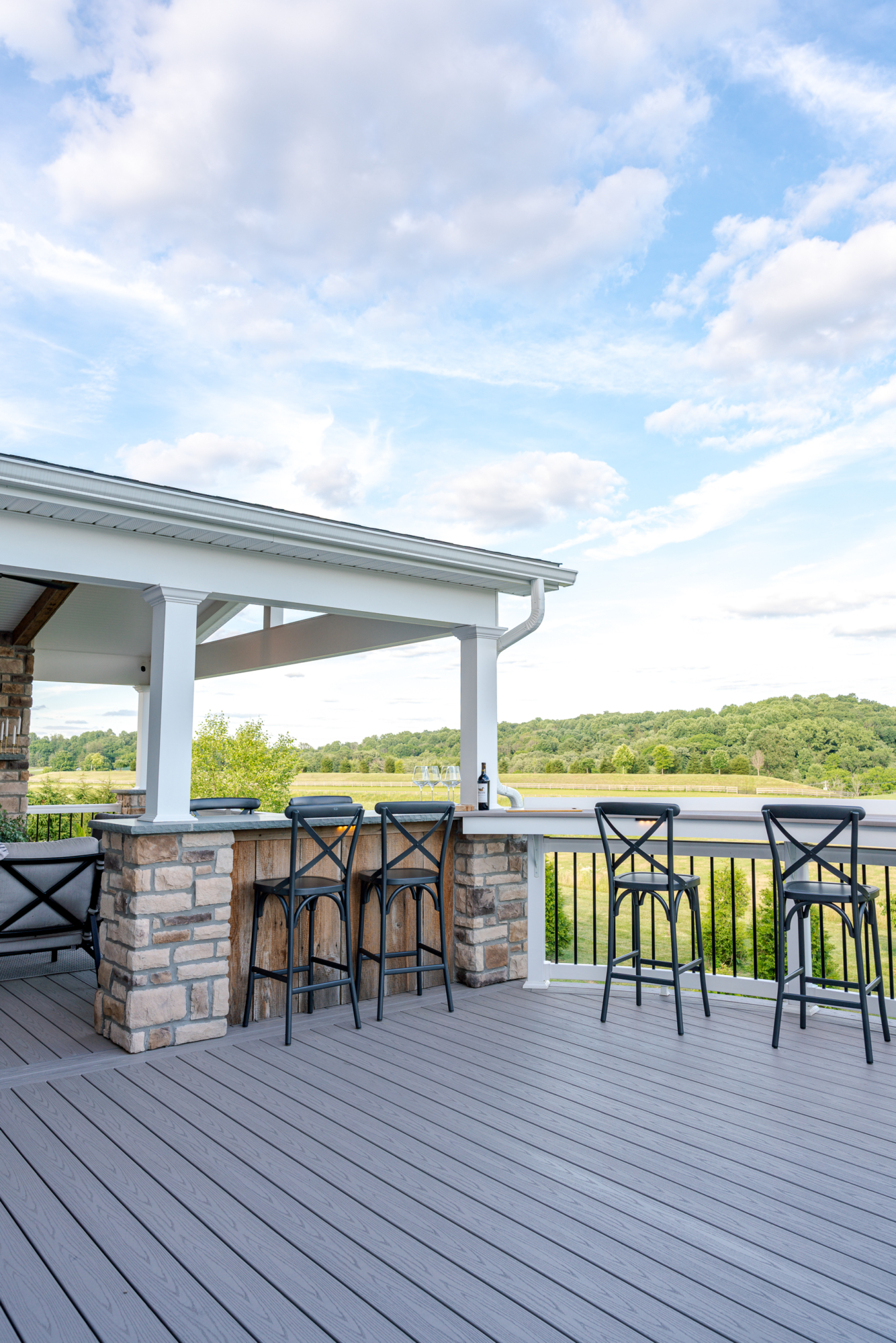 image of a deck in west bradford pa built by integrous fences and decks featuring a roof area a curved deck board bar timbertech decking and white vinyl railing with black aluminum balusters