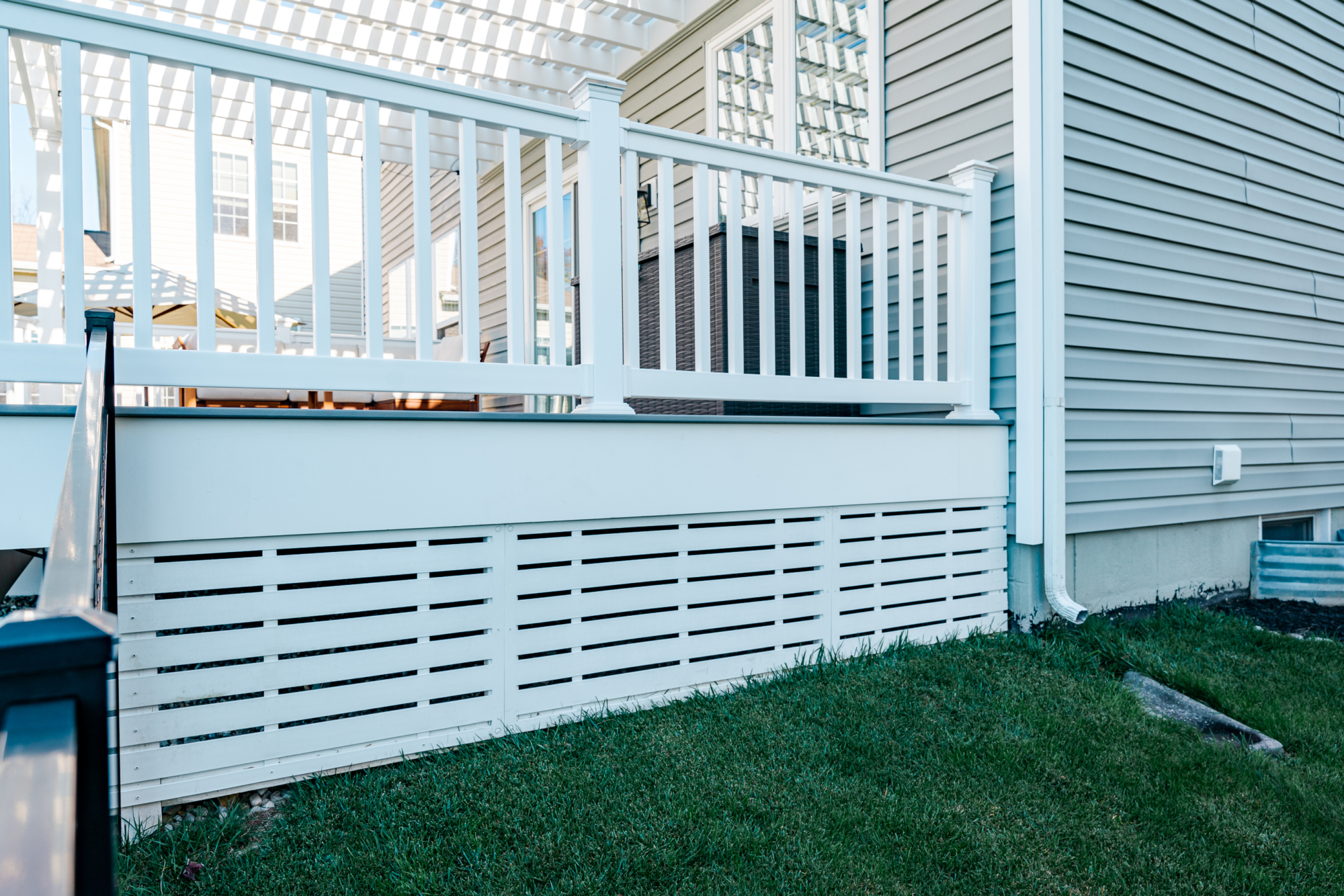 image of a deck and patio in downingtown pa built by integrous fences and decks featuring a white vinyl pergola timbertech decking white vinyl railing paver patio and sitting wall around the yard is a black aluminum fence