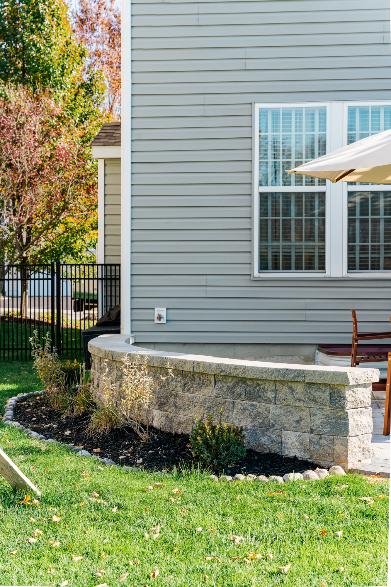 image of a deck and patio in downingtown pa built by integrous fences and decks featuring a white vinyl pergola timbertech decking white vinyl railing paver patio and sitting wall around the yard is a black aluminum fence
